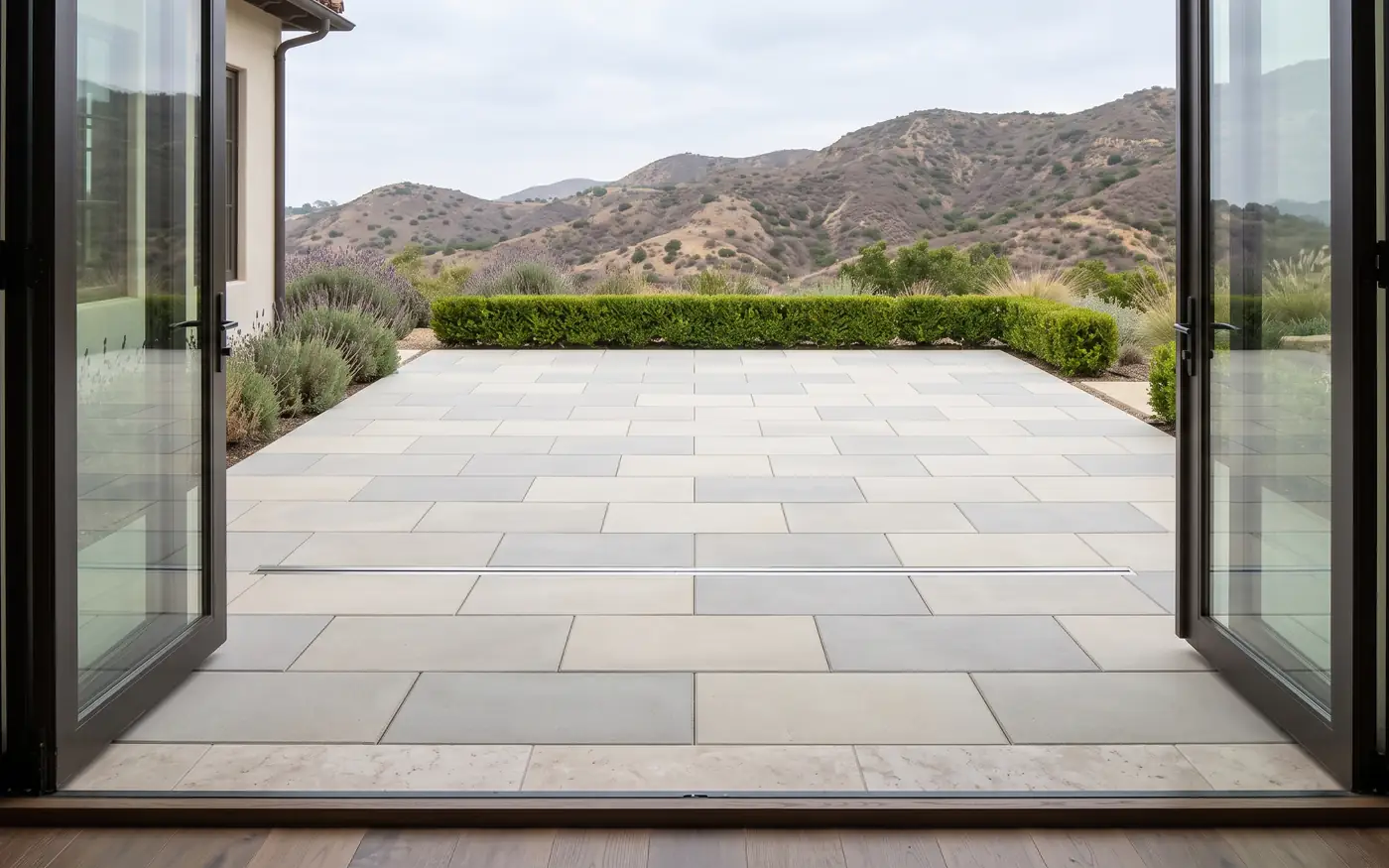 Pale gray paver terrace level with a pair of open glass doors, with a slim slot drain across it