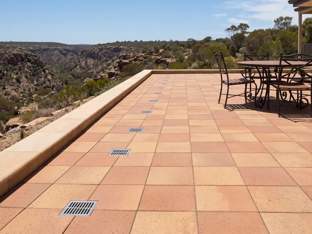 Terracotta paver terrace with flush drain grates, a table and a canyon view