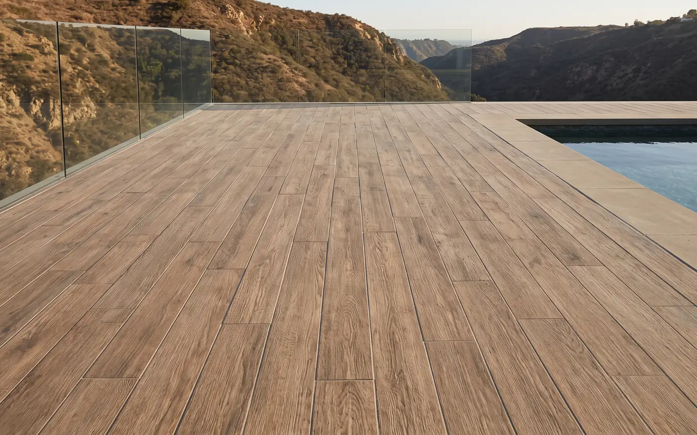 Wood-look porcelain planks with staggered joints on a pool terrace behind a glass railing